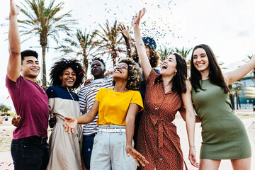 Young multiracial hipster people having fun in summer party celebration - Group of young friends laughing and celebrating all together while throwing coloured confetti at weekend event outdoors