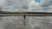 Aerial View Of Beige Salt Lake. Woman In A Dress Walks On The Water As If On A Mirror. The Water Of The Lake Reflects The Blue Sky And Floating Clouds. TUnique Nature. Deserted