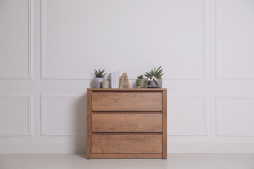 Wall Mural - Books and beautiful plants on wooden chest of drawers near white wall indoors