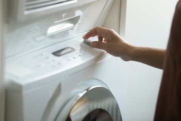 Crop close up of Indian woman turn on modern washing machine doing laundry on weekend at home. Ethnic female renter or housewife switch program on electronic clothing washer. Technology concept.