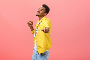 Being carried away with happiness and positive emotions. Portrait of joyful stylish happy dark skinned guy with afro haircut dancing pointing at camera with hand and smiling happily