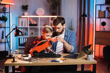 Little Caucasian Boy Soldering Remote Controlled Toy Car While His Father Controlling Process Near. Bearded Man Spending Time With Son Usefully At Home.