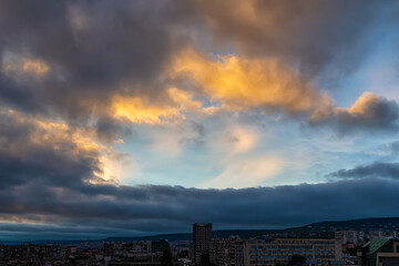 Wall Mural - Dark rain clouds are approaching the city and covering the clear blue sky at evening. Clear sky is visible through the gap in the dark gloomy clouds. Dramatic landscape. Weather forecast, meteorology.