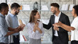 Smiling supportive diverse businesspeople congratulate excited young Caucasian female employee with job promotion or success. Happy multiethnic colleagues greeting woman worker with work achievement.
