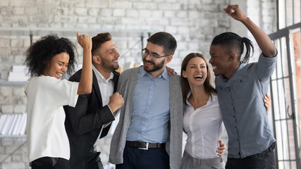 Overjoyed young multiethnic businesspeople have fun celebrate shared business success or victory in office. Smiling multiracial diverse employees feel excited win get good results. Teamwork concept.