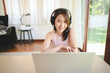 © interstid - Happy smiling Asian woman wearing headset having video conference via laptop at home in living room