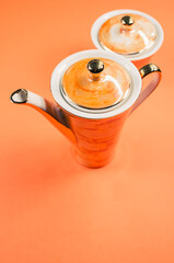 Poster - Close up of an orange covered teapot, a covered cup on an orange isolated background with free space