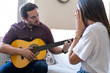 © Irene Castro Moreno - Young and attractive guy playing a romantic song in the guitar to his girlfriend while enjoying a day at home. Woman is surprised and happy listening to his song.