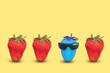 Creative trendy idea with outstanding blue strawberry with goggles and fresh ripe strawberries on yellow background.
