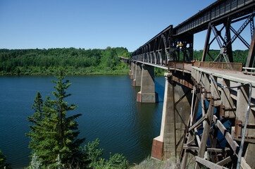 Beautiful summer day with a rusted metal bridge over a clear blue lake surrounded by lush greenery