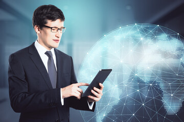 Poster - Attractive young european businessman using tablet on blurry office interior background with polygonal globe hologram. Communication and global business concept. Double exposure.