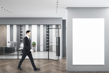 Sticker - Business man walking in modern concrete glass office interior with empty white mockup poster, daylight, equipment and wooden flooring. Workplace design concept.