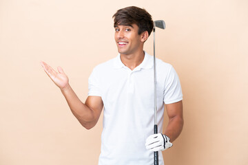 Wall Mural - Young golfer player man isolated on ocher background extending hands to the side for inviting to come