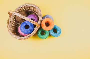 Canvas Print - Pile of colorful textile balls of wool in a wicker basket on yellow background with a copy space