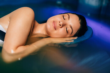 Beautiful woman floating in tank filled with dense salt water used in meditation, therapy, and alternative medicine. .