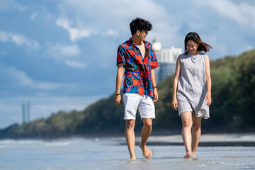 Wall Mural - Happy Asian people on beach travel vacation. Young couple holding hand and walking together on the beach in summer sunny day. Boyfriend and girlfriend enjoy and having fun outdoor lifestyle activity.