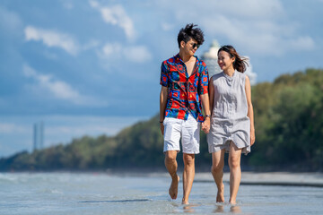 Wall Mural - Happy Asian people on beach travel vacation. Young couple holding hand and walking together on the beach in summer sunny day. Boyfriend and girlfriend enjoy and having fun outdoor lifestyle activity.