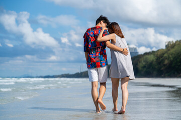 Wall Mural - Happy Asian people on beach travel vacation. Young couple holding hand and walking together on the beach in summer sunny day. Boyfriend and girlfriend enjoy and having fun outdoor lifestyle activity.