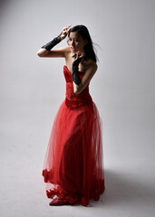 Poster - Full length  portrait of beautiful young asian woman wearing red corset and ornate gothic queen crown. Graceful standing posing  isolated on studio background.