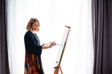 Creative woman painting on canvas near window