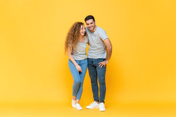 Full length portrait of young happy interracial millennial couple holding each other and laughing in isolated yellow studio background