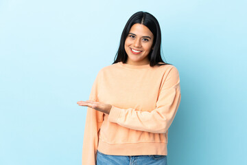 Wall Mural - Young latin woman woman isolated on blue background presenting an idea while looking smiling towards