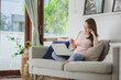 © interstid - Beautiful Asian woman smiling while working at home via laptop notebook in living room