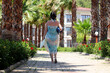 Vacation on tropical  resort. Woman in swimsuit and sarong walking on background of palm trees and villa buildings