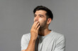 Shocked young Caucasian man looking up and thinking with hand cover mouth on light gray studio background