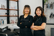 © twinsterphoto - Portrait of team of happy successful young Asian hairstylist standing wearing apron and spectacles with folded hands smiling while looking at camera