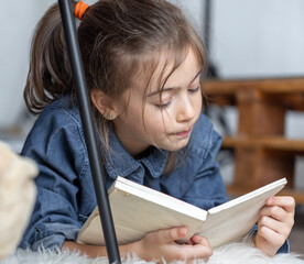 Poster - An elementary school student reads a book at home, lying on the floor.