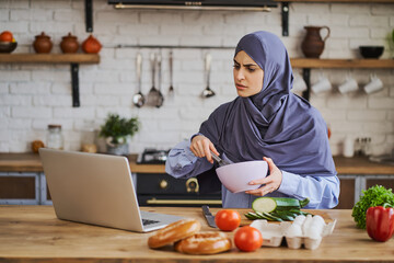 Wall Mural - Arabian woman watching a cooking tutorial and whipping with a whisker