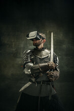 Portrait Of One Brutal Bearded Man, Medeival Warrior Or Knight In VR Glasses With Sword Over Dark Background.