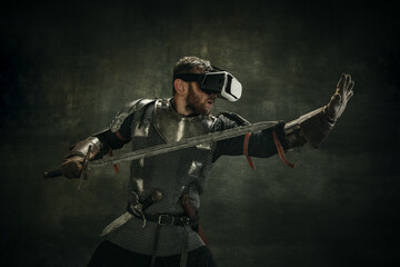 Wall Mural - Portrait of one brutal bearded man, medeival warrior or knight in VR glasses with sword over dark background.