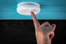 Close Up Smoke Detector On A Ceiling. Woman's Finger Presses The Test Button. Smoke, Fire Alarm