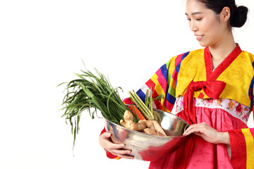 Asian women wearing brightly colored hanboks holding a bowl of fresh vegetables to make kimchi Korean fermented food. Korean national costume concept Asian culinary culture. white background