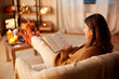 © Syda Productions - halloween, holidays and leisure concept - young woman reading book and resting her feet on table at cozy home