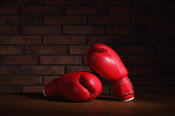 Pair of red boxing gloves on wooden table near brick wall