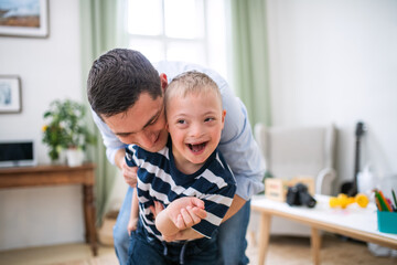 Father with happy down syndrome son indoors at home, having fun.