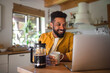 © Halfpoint - Young man with laptop and coffee working indoors, home office concept.
