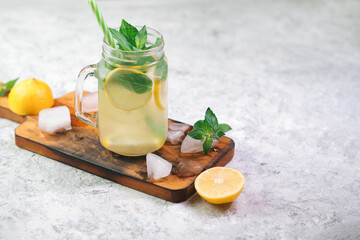 Wall Mural - Summer refreshing ice-cold mojito or lemonade with lemon and mint on a stone white table