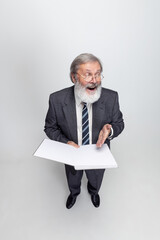 High angle view of elderly gray-headed man, professor, teacher posing isolated on gray studio background. Concept of professional occupation, job, education and motivation.