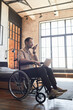 © Seventyfour - Vertical full length portrait of modern adult man in wheelchair speaking by smartphone at home in designer interior