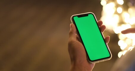 over the shoulder view of hand using green screen smart phone with beautiful golden bokeh at night