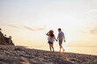 © ViDi Studio - Full body back rear view young couple two friends family man woman in white shirt clothes hold hands walk stroll together at sunrise over sea beach ocean outdoor exotic seaside in summer day evening.