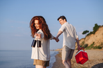 Wall Mural - Back view young couple friend family man woman in white clothes show beer bottle picnic bag refrigerator hold hands walk rest together at sunrise over sea beach outdoor seaside in summer day sunset.