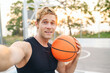 © ViDi Studio - Close up happy cool young sporty sportsman man in black sports clothes training do selfie shot pov on mobile phone hold ball play at basketball game playground court Outdoor courtyard sport concept