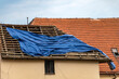 The storm damaged the attachment of the covered tarp on the roof. Installation of a protective tarpaulin on the roof of the house under reconstruction.