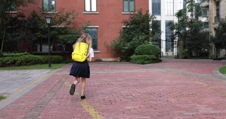happy little caucasian blonde girl seven years old in uniform with yellow backpack running back to s