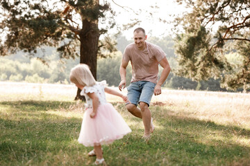 Wall Mural - Father is playing with little daughter on summer day. Portrait dad with child together. Daddy, little daughter outdoors. Young father with baby girl walk in park. Family holiday in garden or forest.